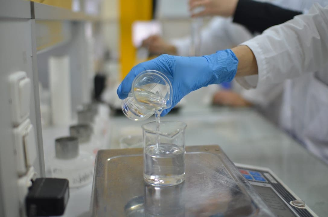 A medical lab scientist's glove pouring liquid into a test cup.