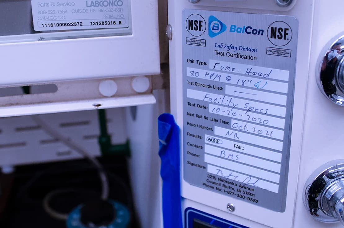 Fume hood certification label showing BalCon Lab Safety Division test results and compliance with NSF standards.