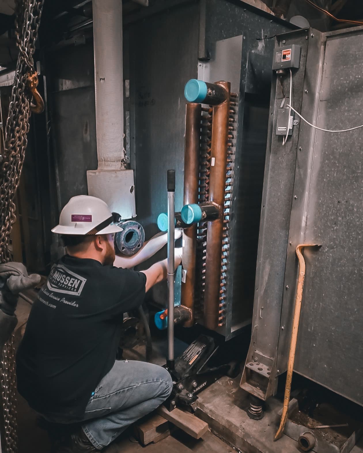 HVAC technician wearing safety gear installing a new copper coil inside a large air handling unit.