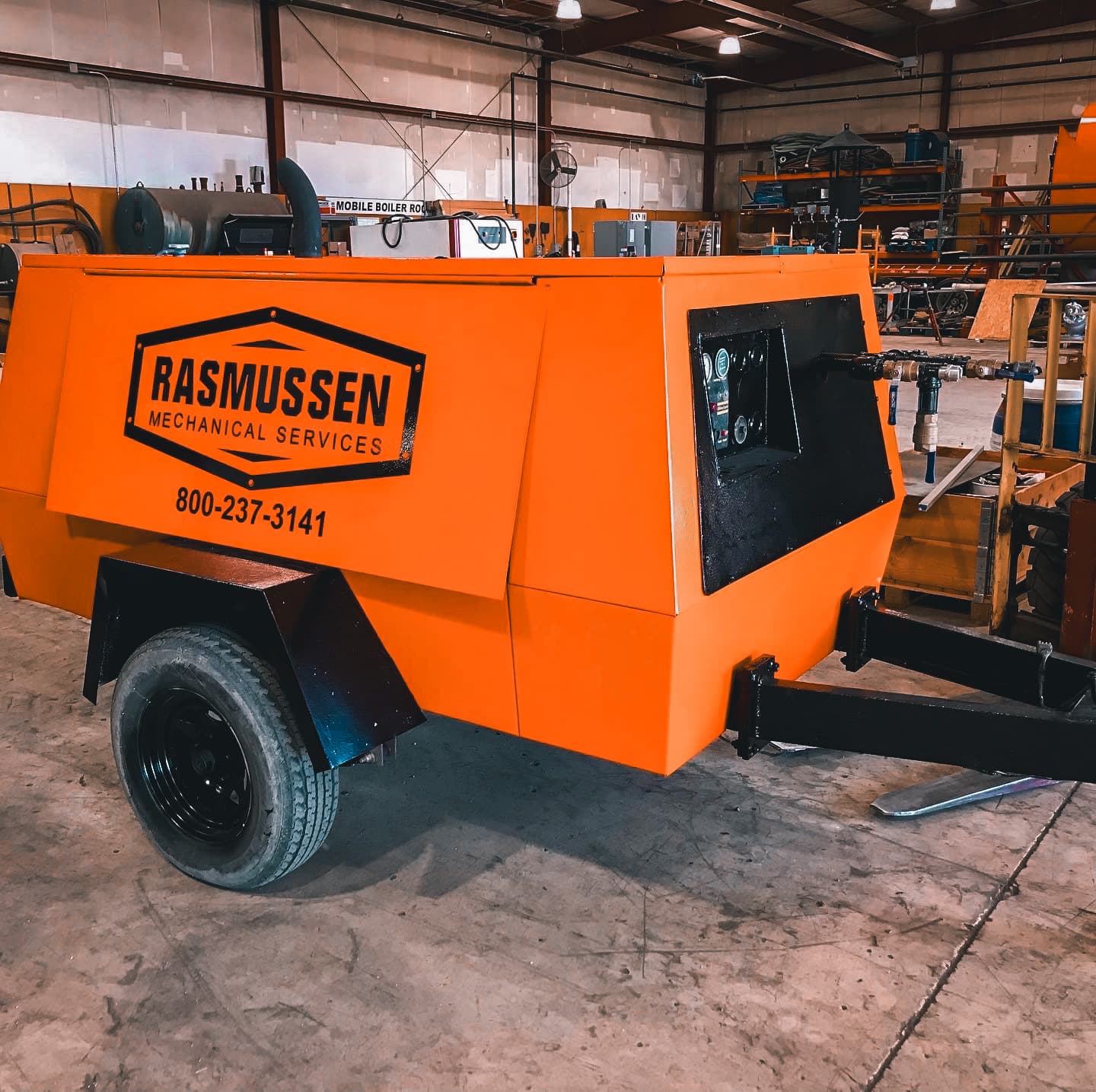 Bright orange Rasmussen Mechanical trailer-mounted air compressor parked in a service bay.